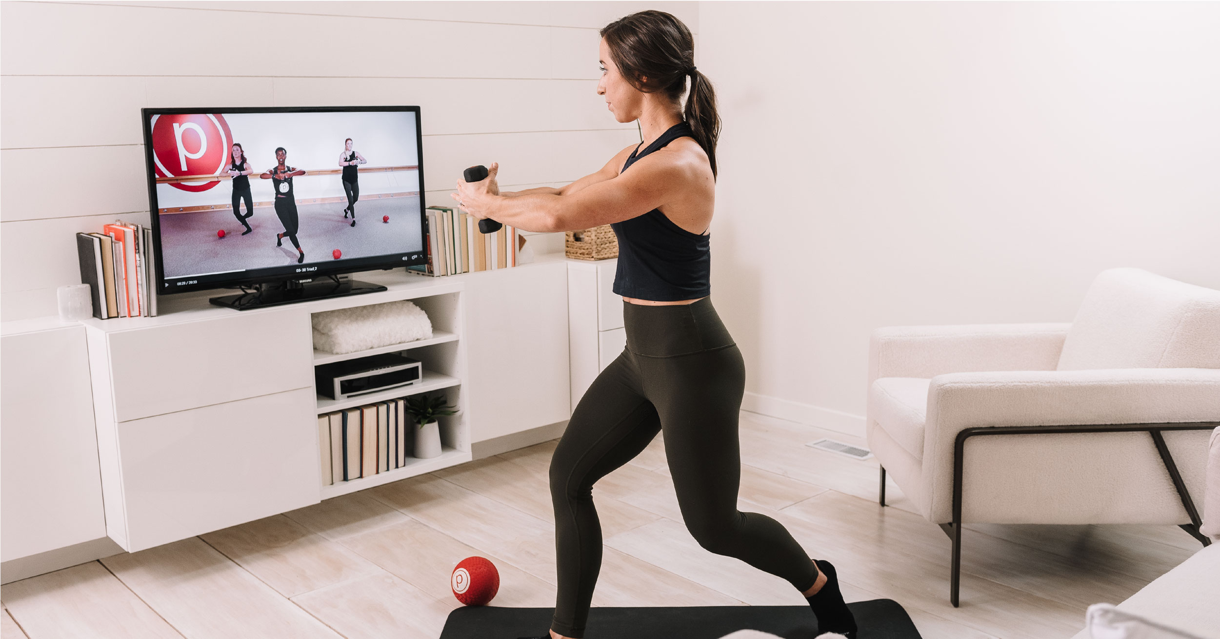 Person holding dumbbell while following along to Pure Barre workout on the TV 